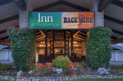 Exterior view of the Inn at Pasatiempo entrance, featuring signage for "Inn at Pasatiempo" and "Back Nine Grill & Bar," with lush plants and colorful flowers in front of the building.